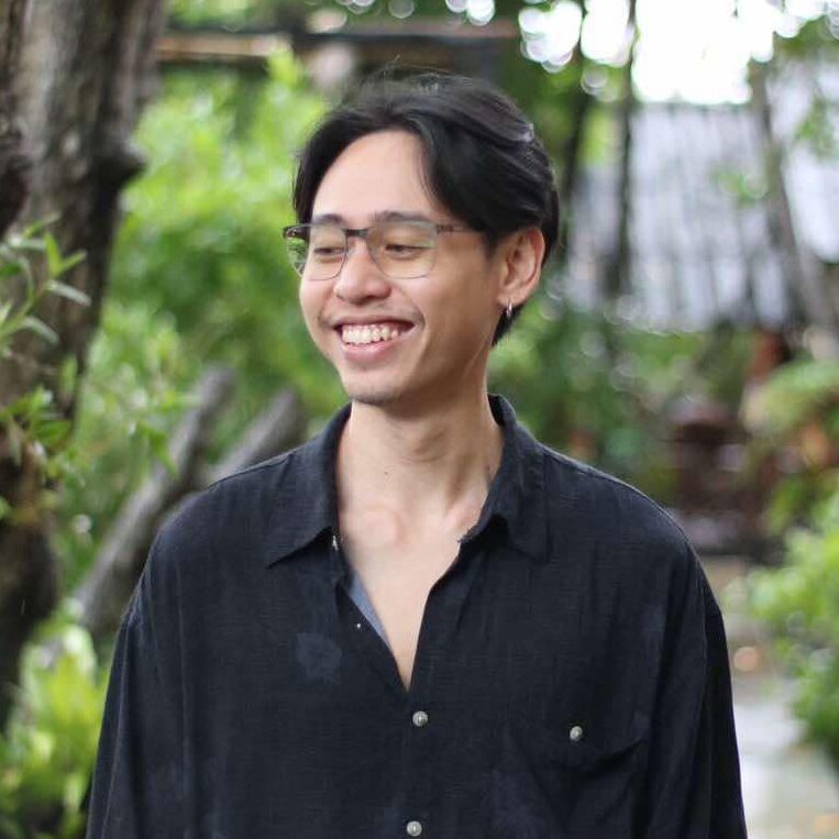 Chetniphat Koawthong นักพัฒนาเว็บไซต์ WordPress ฟรีแลนซ์ ยืนยิ้มในสวนธรรมชาติ สวมเสื้อเชิ้ตสีดำและแว่นตา สื่อถึงความเป็นมืออาชีพและเป็นกันเอง